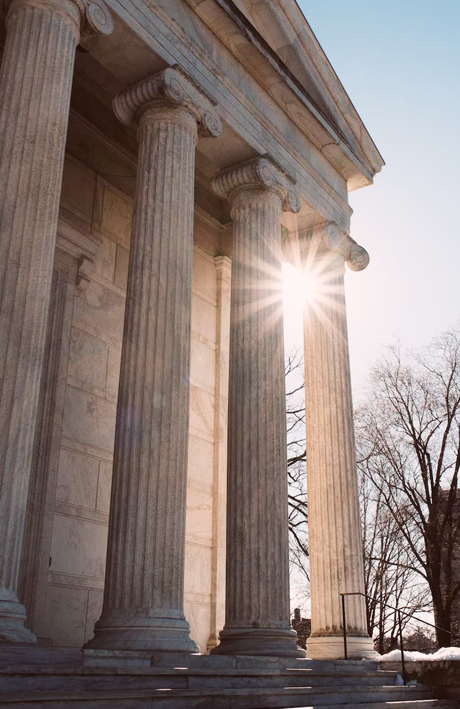 A tall building with pillars and sunshine in view